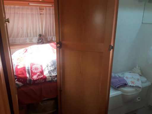 Ein kleiner Raum mit einem Bett, das mit einer Decke bedeckt ist, und einer angrenzenden Toilette.